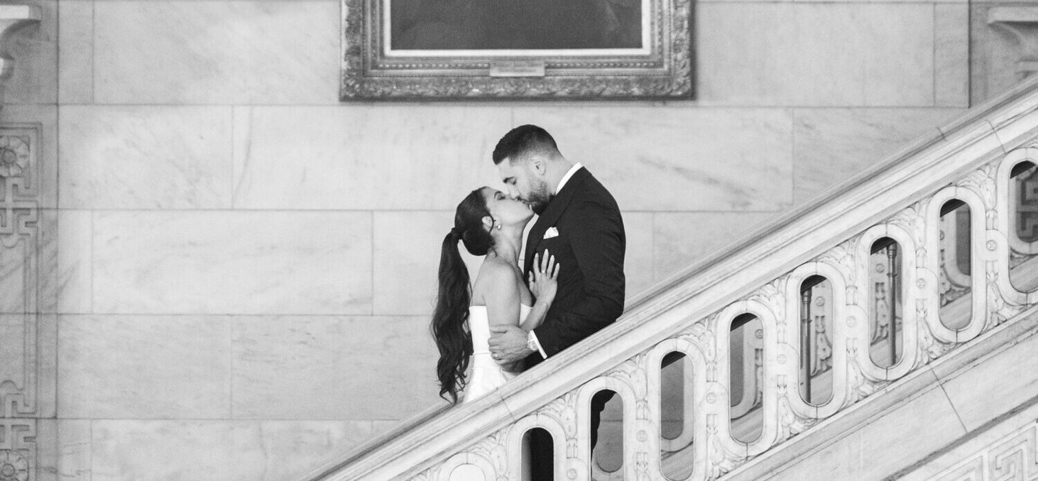 A bride and groom kissing on the staircase in front of a painting at New York Public Library for their wedding photos.